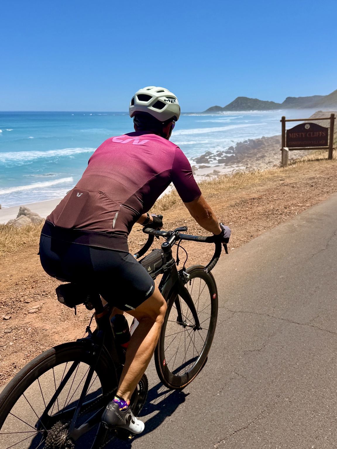 Road cyclist riding beside the turquoise ocean at Misty Cliffs
